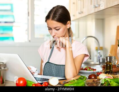 Frustrierte junge Frau mit ihrem Laptop in der Küche Stockfoto