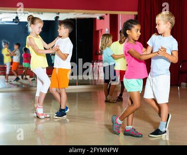 Eine Gruppe fröhlich lächelnder Kinder, die versuchen, mit dem Partner im Klassenzimmer zu tanzen Stockfoto