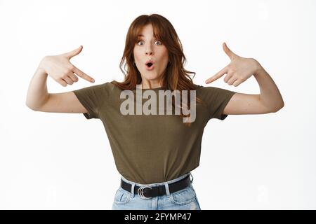 Portrait of surprised girl Student pointing fingers down at Center, showing Logo Banner and keuchen stauned, Check out special promo Offer in Shop Stockfoto