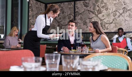 Elegantes Paar sitzen am Tisch im Restaurant im Gespräch mit junge Kellnerin Stockfoto