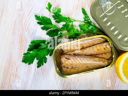 Appetitliche scomber-Filets in Sonnenblumenöl in offener Blechdose auf Holztisch mit frischer Petersilie und Zitrone Stockfoto