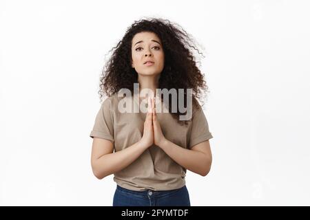 Hilfe bitte. Bettelendes Mädchen, das um Gunst bittet, die Hände im Gebet hält und Coy sucht, um Rat bittet, etwas braucht, gegen Weiß steht Stockfoto