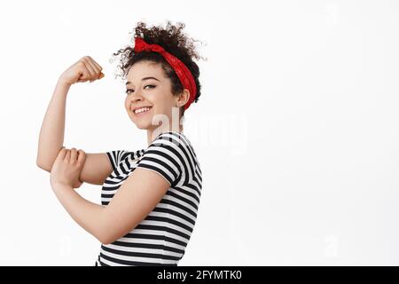 Wir können es schaffen. Frauenmacht und Feminismus Konzept. Starke und selbstbewusste Brünette Mädchen zeigt ihren Arm Muskel, Flex Bizeps und lächelnd stolz, stehend Stockfoto