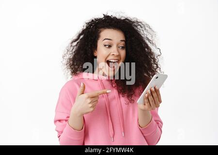 Porträt der aufgeregt Brünette Frau Schrei aus Freude, zeigen und Blick auf Handy-Bildschirm, Check-out awesome Promo-Angebot online, stehend Stockfoto