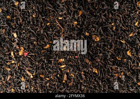Selektiver Fokus. Lebensmittelhintergrund. Natürlicher schwarzer Tee zum Brauen mit Blättern und Blumen. Draufsicht, mit tiefen Schatten. Textur. Makro, Copyspace Stockfoto