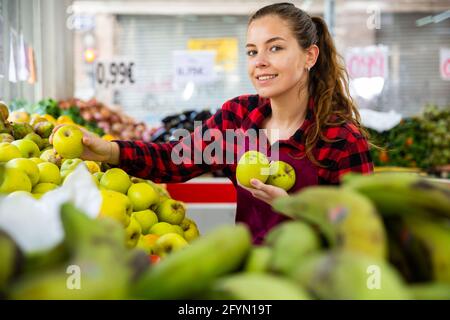 Porträt einer positiven jungen Verkäuferin, die Äpfel auf der Theke auslegt Stockfoto