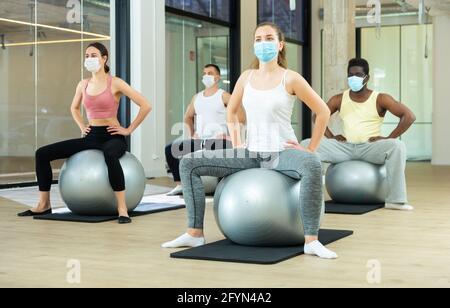 Gruppe von sportlichen Menschen in Schutzmasken, die Übungen an Fitballs während des Pilates-Kurses im Fitnesscenter machen. Gesunde Lebensweise und Pandemie precauti Stockfoto