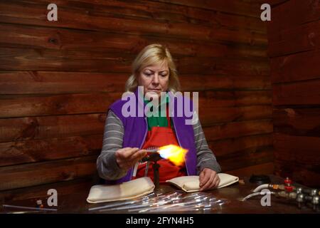 Weihnachtsdekorationen. Weibliche Glasbläser, die Glasrohling mit einem Gasbrenner erwärmt. 10. Dezember 2018. Kiew, Ukraine Stockfoto