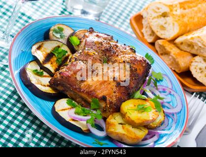 Gegrillte Schweinerippchen Rack garniert auf weiße Platte mit gebackenen Kartoffeln und Auberginen und Frische rote Zwiebel Stockfoto