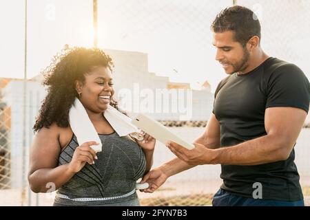 Personal Trainer arbeitet mit kurvigen Frau, während sie ihre Konstruktion Mit digitalem Tablet während des Trainings - Sport People Lifestyle Konzept Stockfoto