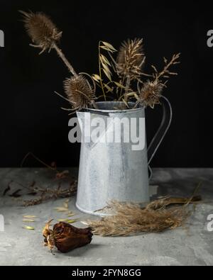 Zusammensetzung aus Blumen und getrockneten Pflanzen, von denen ein Teil in einer Zinnvase Stockfoto