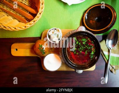 Herzhaftes rotes Borscht in Fleischbrühe serviert mit frisch gebackenem Pampushky, gehacktem salo mit Knoblauch und saurer Rahm. Ukrainische Küche Stockfoto