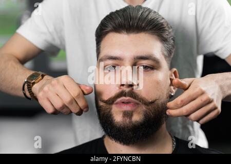 Fixieren der Schnurrbart-Form mit Wachs. Das Ergebnis eines Haarschnitts in einem Friseurladen Stockfoto