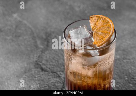 Cocktail in Glas mit Cola, Alkohol, Eis, dekoriert getrocknete Orange auf grauem Hintergrund Stockfoto