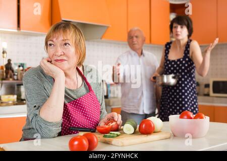 Älterer Mann und junge Frau schimpfen seine Frau in der Küche Stockfoto