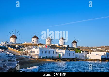 Wunderschöne Aussicht auf die berühmten traditionellen weißen Windmühlen auf dem Hügel, Mykonos, Griechenland. Weiß getünchte Häuser, Sommer, Morgen, Meer, ikonisches Ziel Stockfoto