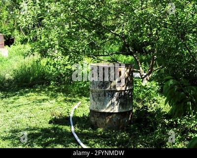 Im Sommer steht im Garten ein Metallwasserfass Stockfoto