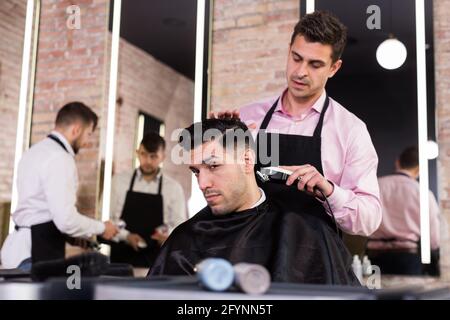 Professionelle friseur Mann tun Styling hübscher Kerl mit elektrischer Haarschneider bei Friseur Stockfoto