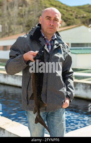 Stolz männliche Inhaber der Fischzucht in der Nähe von Pools mit frischen Störe in den Händen Stockfoto