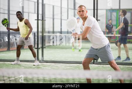 Porträt eines fokussierten Padel-Spielers, der während eines Freundschaftsspiels auf dem engen Platz mit zwei Händen auf die Hinterhand trifft Stockfoto