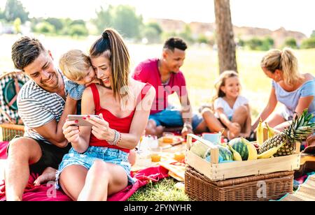 Glückliche multiethnische Familien spielen mit dem Telefon auf pic nic Gartenparty - Freude und Liebe Lifestyle-Konzept mit gemischten Rennen Menschen Spaß zusammen haben Stockfoto