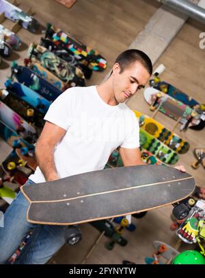 Netter junger Mann, der Skateboard im Laden wählt Stockfoto