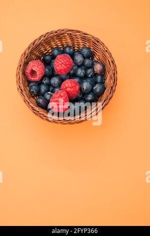 Draufsicht auf Heidelbeeren und Himbeeren in einem Korb auf orangefarbenem Hintergrund Stockfoto