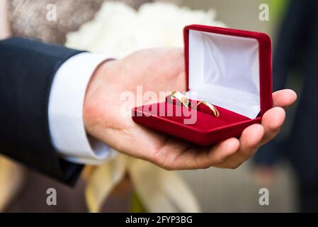 Eheringe in einer Schachtel, die in einer männlichen Hand gehalten wird. Symbol „Ehe“. Vorbereitung auf die Hochzeit. Stockfoto