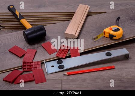 Planken von Laminatboden und Ausrüstung oder Werkzeuge, um sie zu installieren, Hammer, Brecheisen, Distanzstücke, Hammer und Meter. Selektiver Fokus. Stockfoto