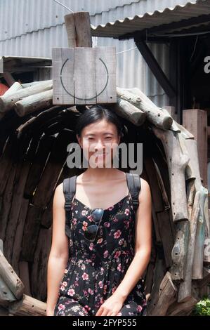Eine lächelnde chinesin, die auf einem Holzstuhl auf dem historischen Kausteg in georgetown in Penang Malaysia sitzt. Stockfoto