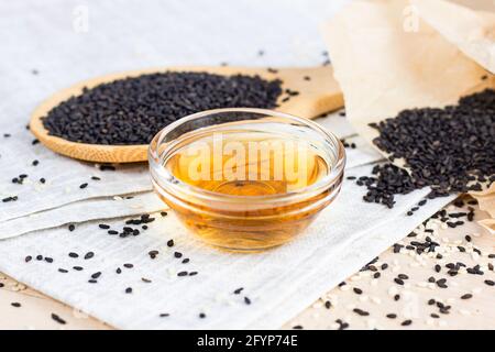 Schwarze Sesamsamen in einem Holzlöffel und Öl auf hellem Hintergrund in der Küche. Stockfoto