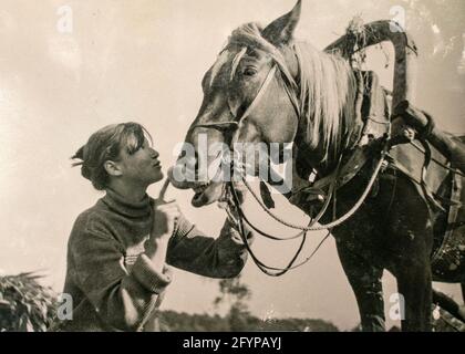 Deutschland - UM 1930er Jahre: Bäuerin und Pferd arbeiten an der Getreideernte. Getreideschocks auf einem Feld. Archivieren Sie Vintage Schwarz-Weiß-Fotografie Stockfoto