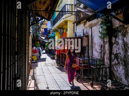 Eine sonnendurchflutete Frau in einem violetten Kleid geht durch eine schmale Gasse in der Chinatown-Gegend von Bangkok, Thailand Stockfoto