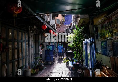 Ein junger Mann zieht am Ende einer sonnenbeschienenen Gasse in der Chinatown-Gegend von Bangkok, Thailand, Waren auf einem Trolley mit. Stockfoto