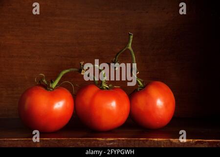 Auf einem Holzregal sind in einem Stillleben-Bild drei Tomaten zu sehen. Stockfoto