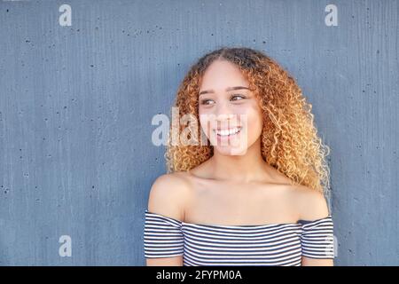 Lächelndes Porträt von Latina Teenager auf grauem Hintergrund. Nahaufnahme eines jungen Mädchens mit glücklichem lockiges Haar. Hochwertige Fotos Stockfoto