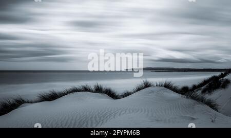 Moody Camber Sands Beach in East Sussex, im Dorf Camber, Großbritannien. Schwarzweißeffekt mit Langzeitbelichtung Stockfoto