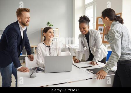 Gruppe von glücklichen jungen, vielfältigen Geschäftsleuten, die sich unterhalten, lustige Ideen austauschen und lachen Stockfoto