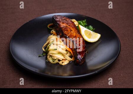 Pasta mit Lachs in Sojasauce und Zitrone auf A Schwarze Platte Stockfoto