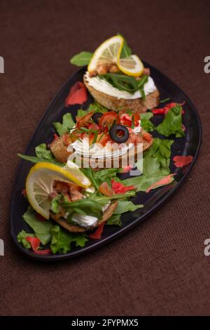 Bruschetta mit Frischkäse und Oliven auf einem schwarzen Teller. Stockfoto