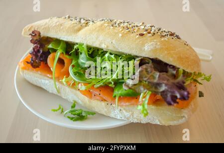 Baguette-Sandwich mit rauchfarbenem Lachsfisch, Rucola-Salat und rotem Eichensalat auf dem Holztisch. Stockfoto
