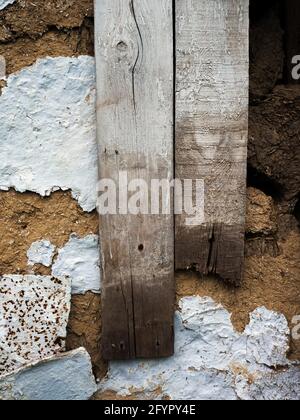 Alte Wand aus Ton mit Brettern. Ein vertikales Bild einer alten Wand mit abblätternder Farbe und genagelten Brettern. Stockfoto