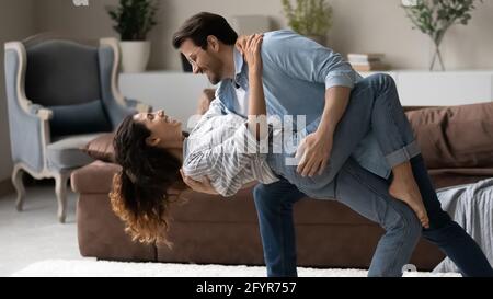 Lächelnde multiethnische Paare tanzen im Wohnzimmer zusammen Stockfoto