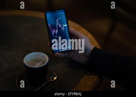 Geschäftsmann überwacht Echtzeit-Aktienmarktdaten auf dem Smartphone, während Draußen sitzen Stockfoto