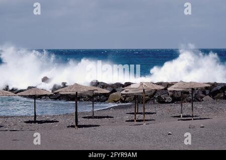 Eine leere Bucht aus Lavasandstrand in Corona Zeiten ohne Menschen und ohne Liegen, aber mit einer Reihe offener Strohschirme. Dahinter hoch, l Stockfoto
