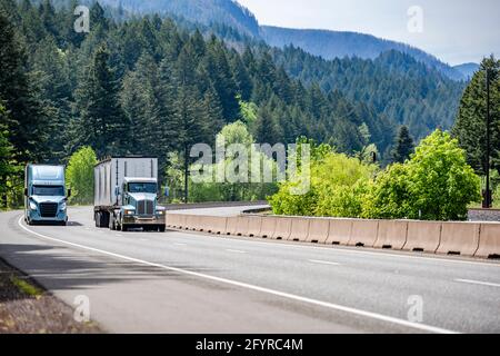 Zwei verschiedene große Rig-Industrie-Sattelschlepper transportieren kommerzielle Ladung in verschiedenen Sattelaufliegern, die nebeneinander laufen highway Road mit Stockfoto