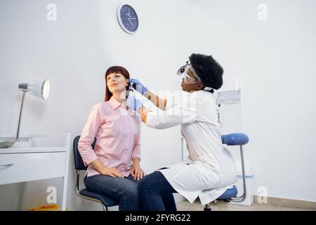 Junge attraktive kaukasische Frau bekommen medizinische Ohruntersuchung in der modernen Klinik. Weibliche Praktizierende, die das Ohr des Patienten untersucht, mit einem Otoskop, in einer Arztpraxis Stockfoto