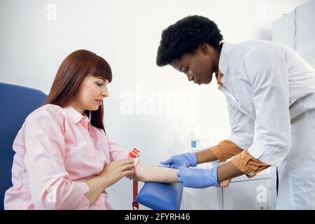 Vorbereitung auf den Bluttest. Schöne junge afrikanische Frau Arzt in weißer medizinischer Uniform bereit, Blutprobe aus der Vene des Patienten zu nehmen Stockfoto