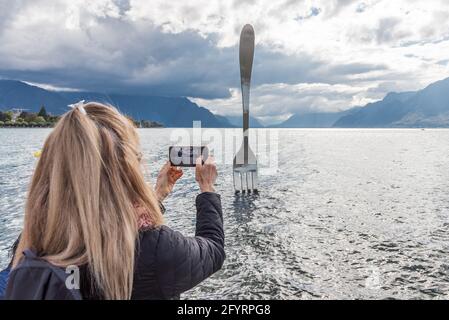 Blonde Frau, die ein Foto von einem Denkmal in der Mitten im Genfersee mit den Alpen im Hintergrund Stockfoto