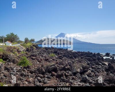 Die vulkanische Felsküste der Insel Faial mit dem Berg Pico am Horizont Stockfoto